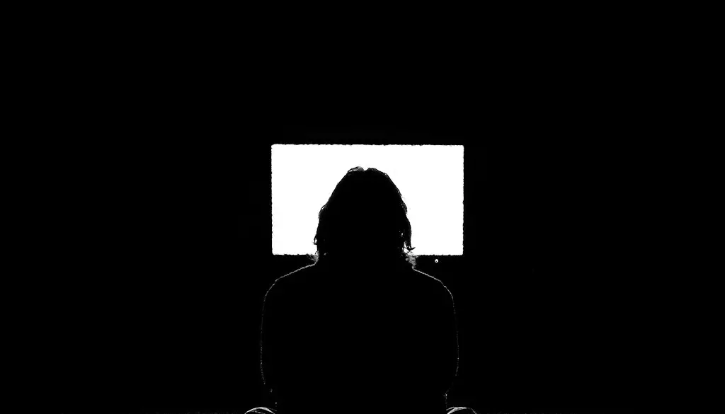 A hand holding a TV remote pointed at a television